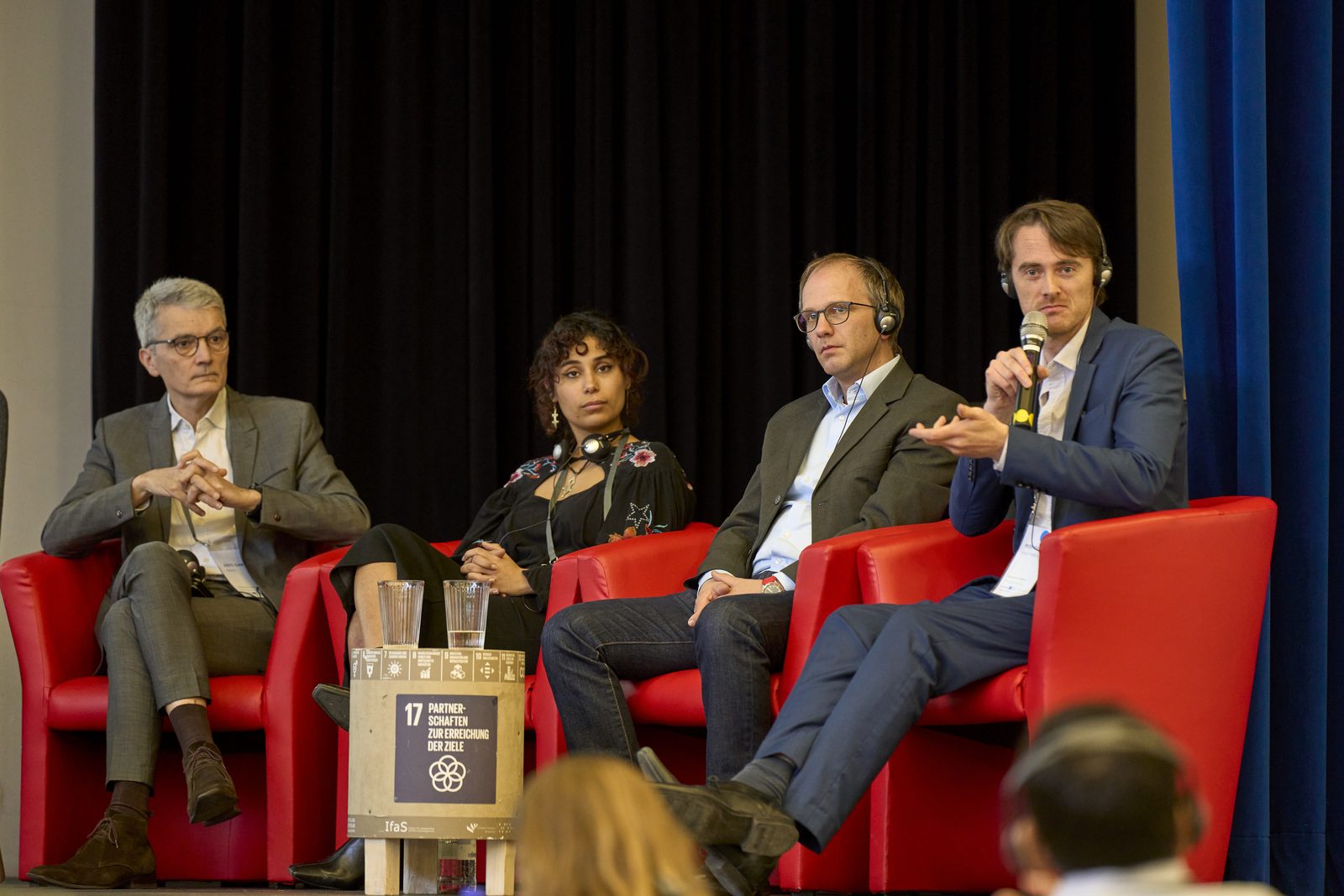 Vier Personen in roten Sesseln auf einer Bühne bei einer Podiumsdiskussion.