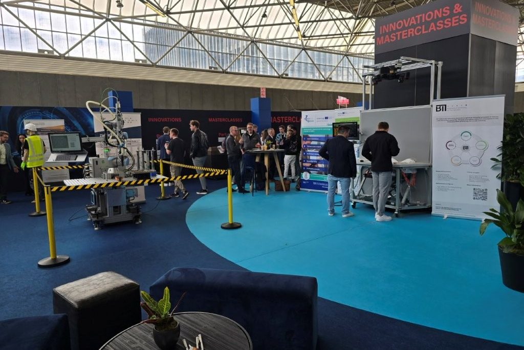 Ausstellungsfläche unter dem Hallendach mit zwei Roboter-Demonstratoren, Roll-ups und Besuchern vor dem Schild Innovations and Masterclasses.