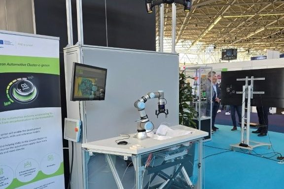 Ein mobiler Arbeitsplatz mit kollaborierendem Roboter, Kameragestell und Bildschirm neben einem Roll-up von PAE-e-green.