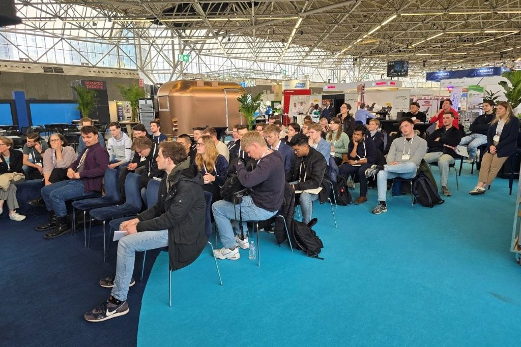Rund vierzig Besucher auf Stühlen in der Messehalle hören einem Vortrag zu.
