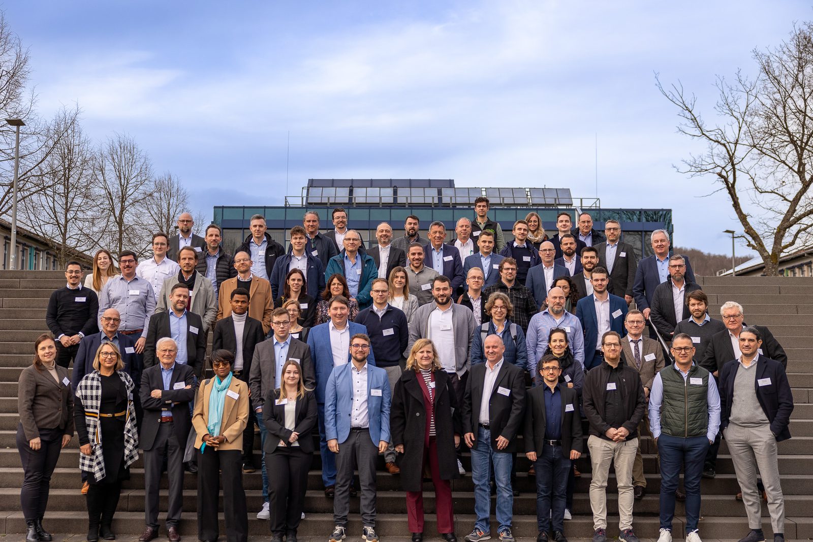 Group photo of about eighty participants on the outdoor steps of the campus.